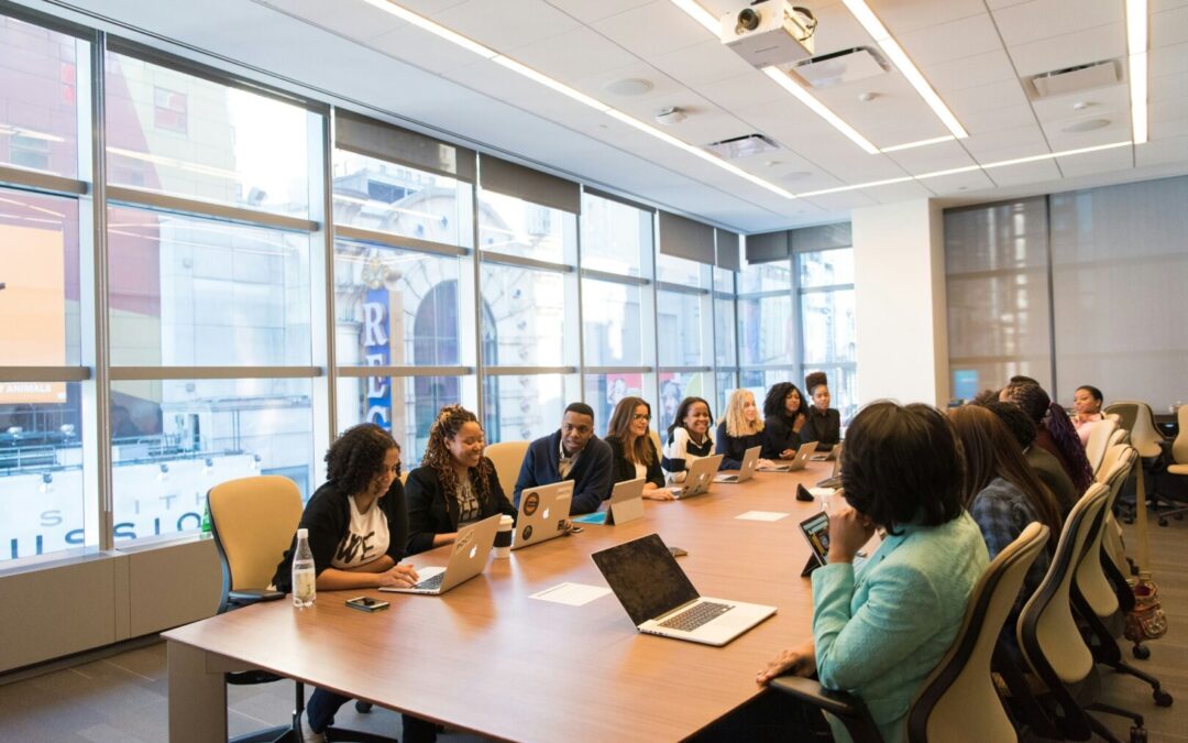 Group of diverse knowledge workers sitting at a large conference room table, chatting casually.